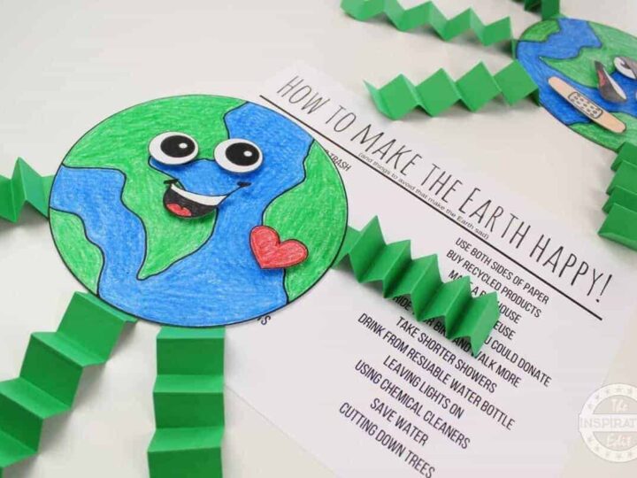 Craft project showing a smiling Earth with googly eyes, a red heart sticker, and accordion-folded green legs. Background shows instructions titled How to Make the Earth Happy with tips for recycling and saving energy.