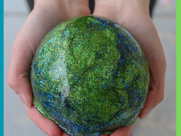 Hands holding a large, glittery ball covered in green and blue sparkles, resembling Earth with a shimmering effect.