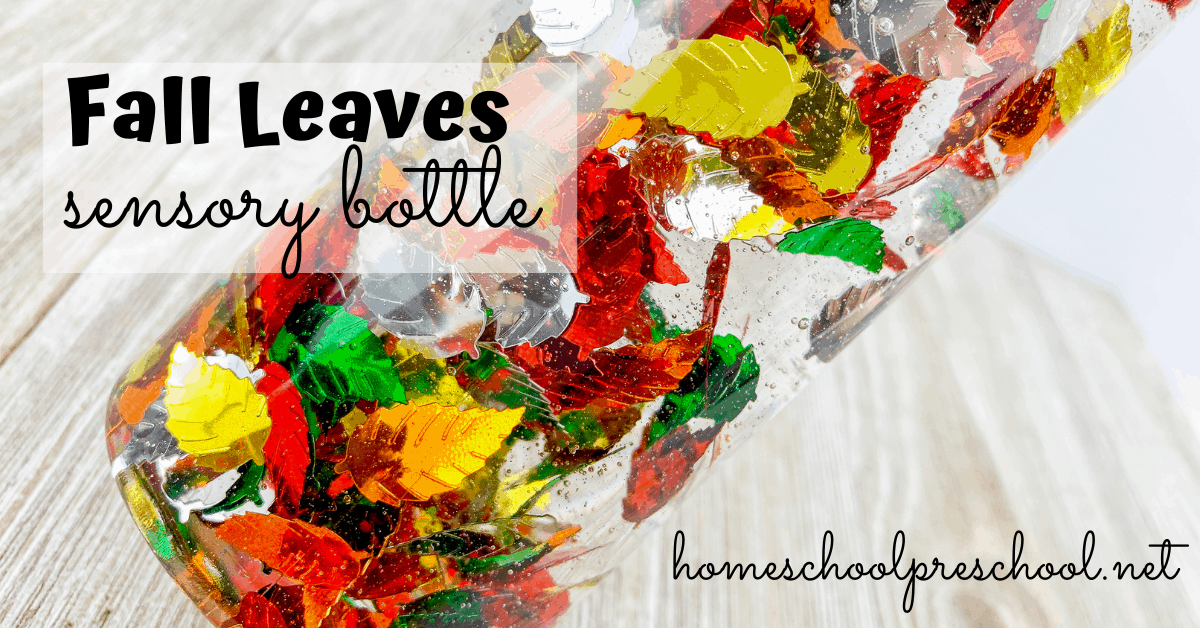 A fall-themed sensory bottle filled with colorful leaves in red, green, yellow, and orange. The bottle is titled Fall Leaves sensory bottle, with homeschoolpreschool.net written below. The bottle lies on a wooden surface.