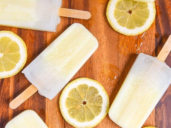 Lemon popsicles arranged on a wooden surface with sliced lemons scattered around, creating a refreshing and summery vibe.