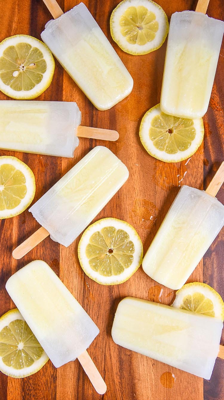 Lemon popsicles arranged on a wooden surface with sliced lemons scattered around, creating a refreshing and summery vibe.