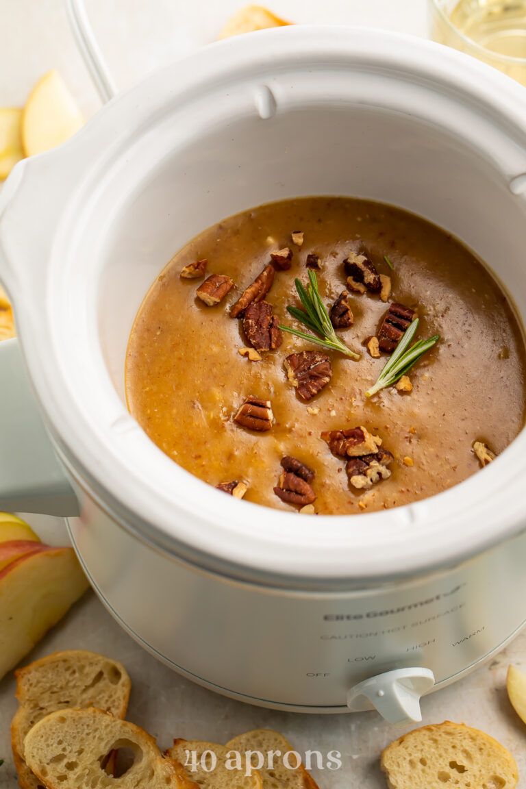 Crockpot baked brie dip topped with preserves and pecans