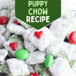 Bowl of Grinch puppy chow with red hearts and green candies, with text Easy No-Bake Grinch Puppy Chow Recipe