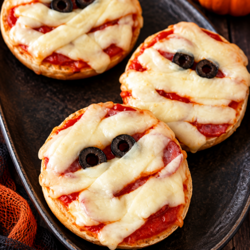 Mummy face pizzas made on bagel halves with pizza sauce, string cheese bandages and black olive eyes