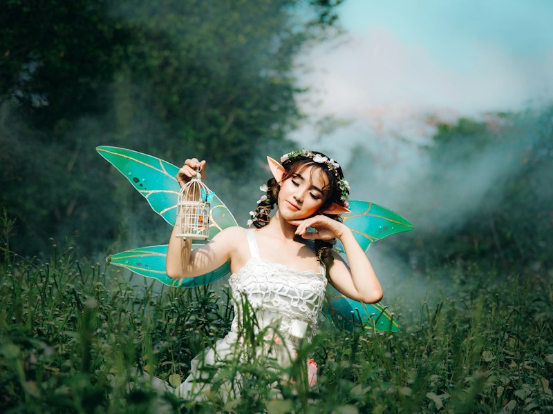 Woman dressed as a fairy with green wings holding a small lantern in a misty forest